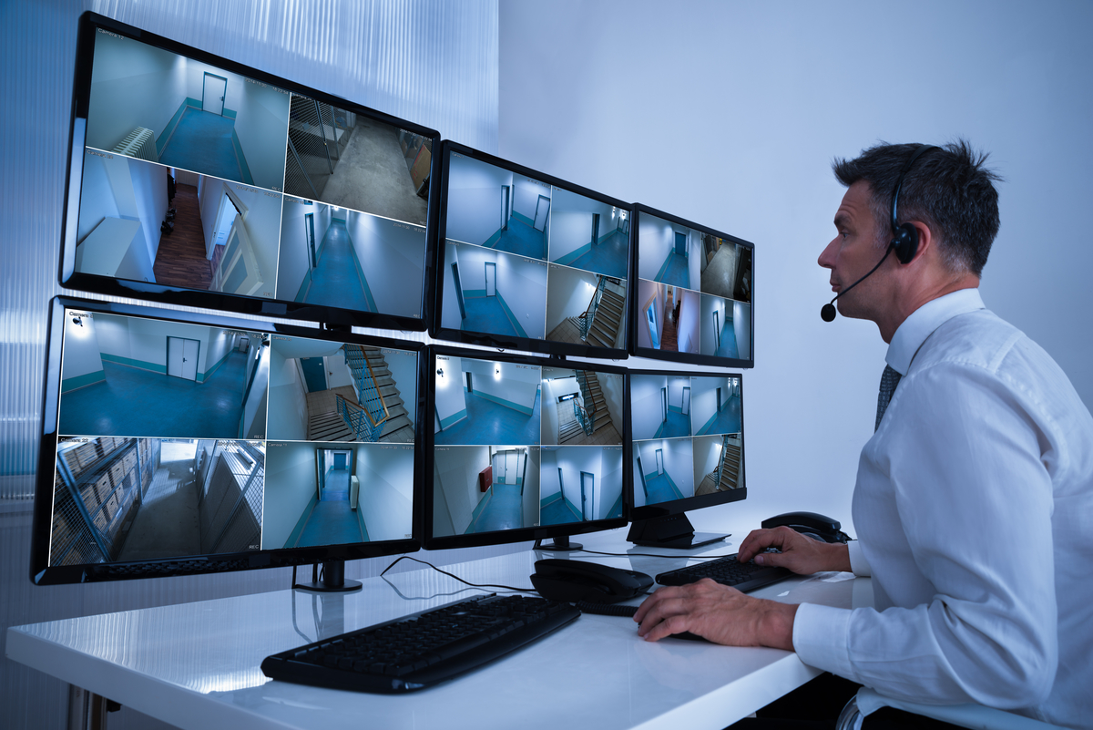 Security System Operator Looking At CCTV Footage At Desk